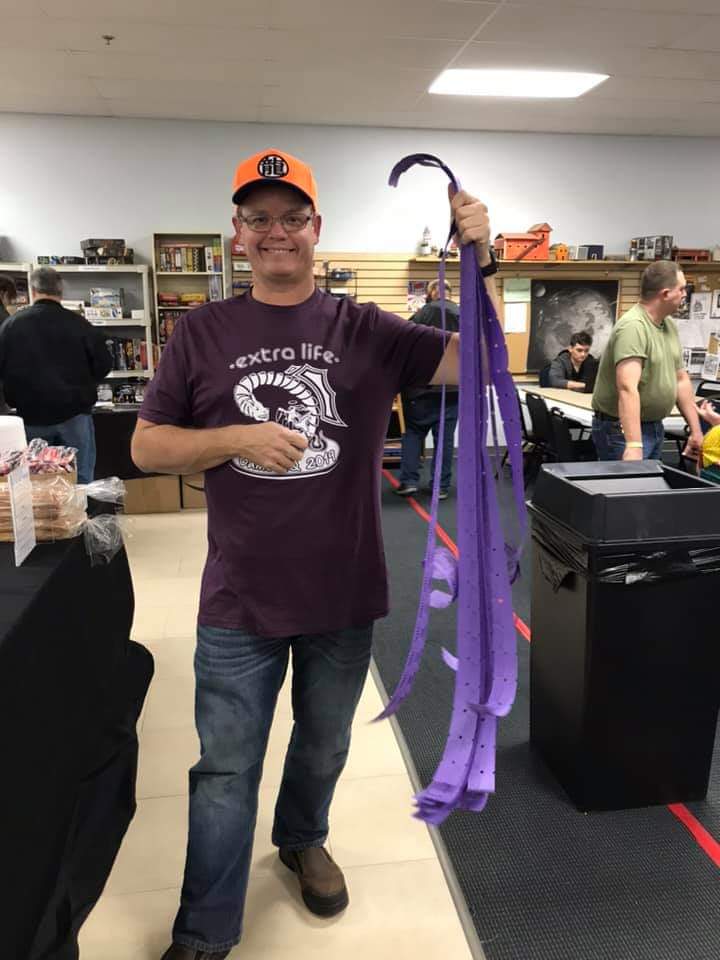 A man wearing a red Extra Life tshirt is holding long strips of raffle tickets up proudly.